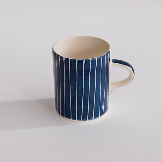 A blue and white coffee mug with sgraffito stripes.
