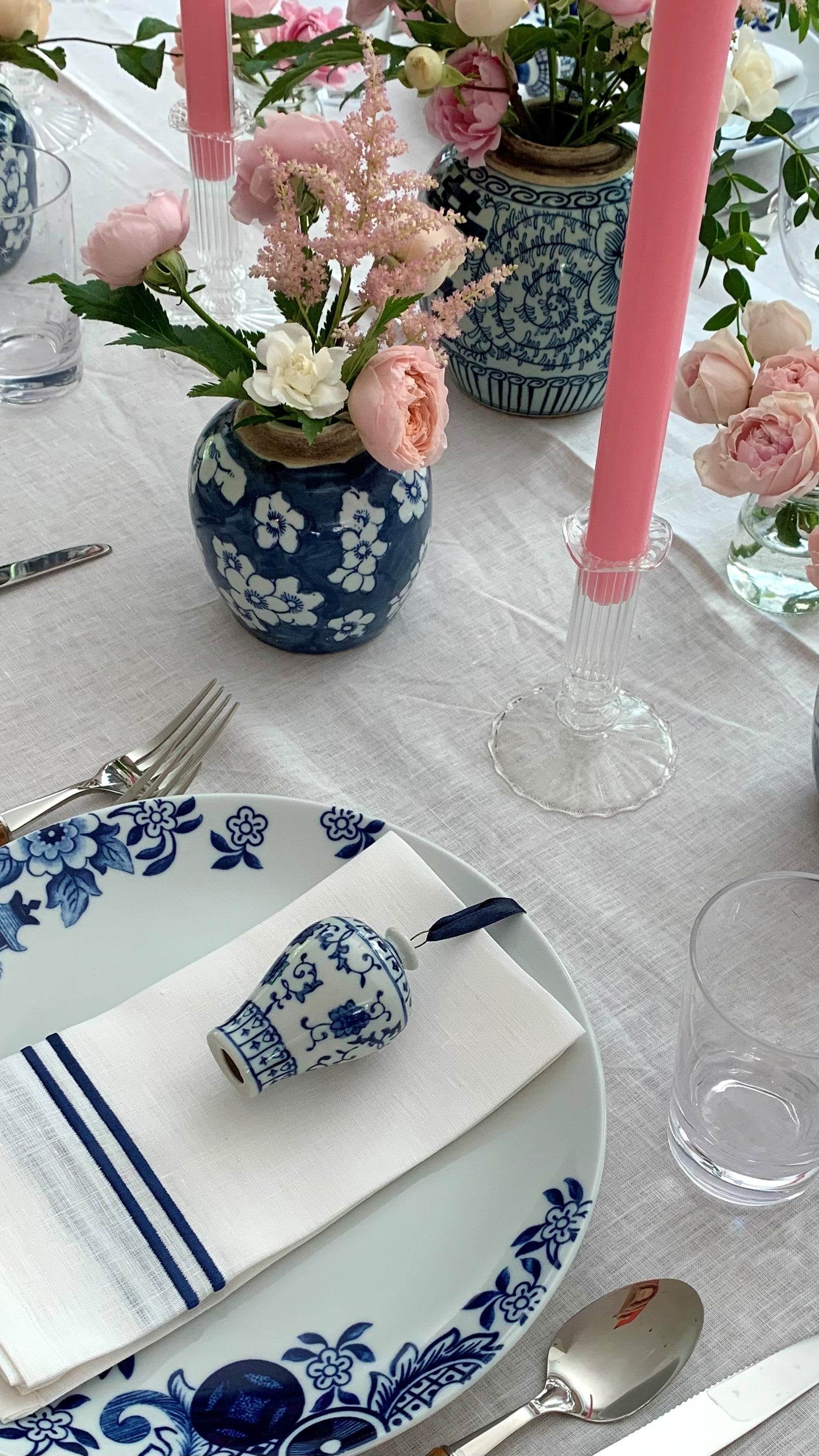 A blue and white tablescape with ginger jars filled with flowers and cherry blossom candles in clear candle holders.