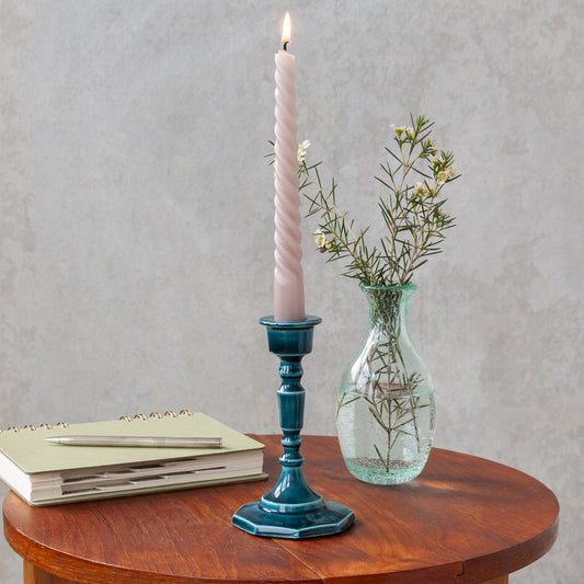 blue enamel candlestick with a pink candle on a table next to a vase of flowers and a book
