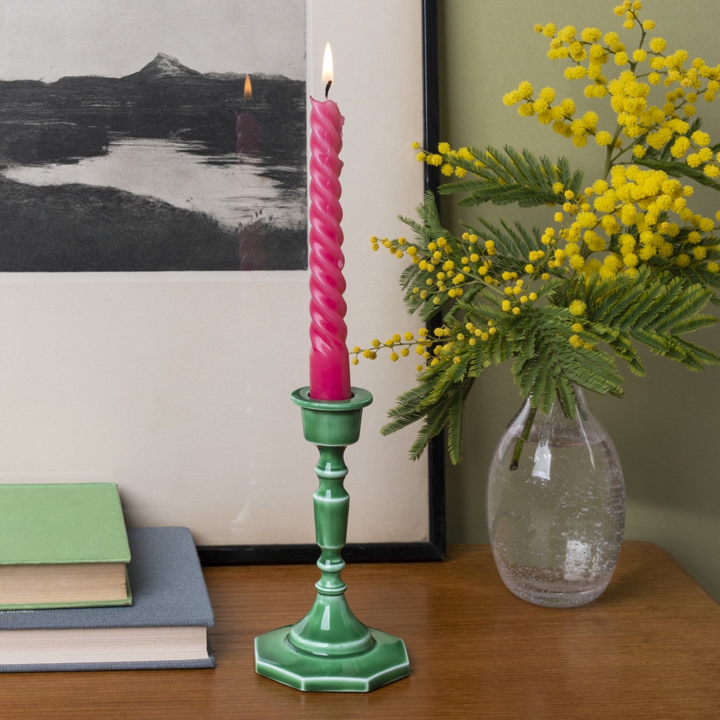 dark green enamel candlestick with a pin candle on a shelf next to a vase of flowers