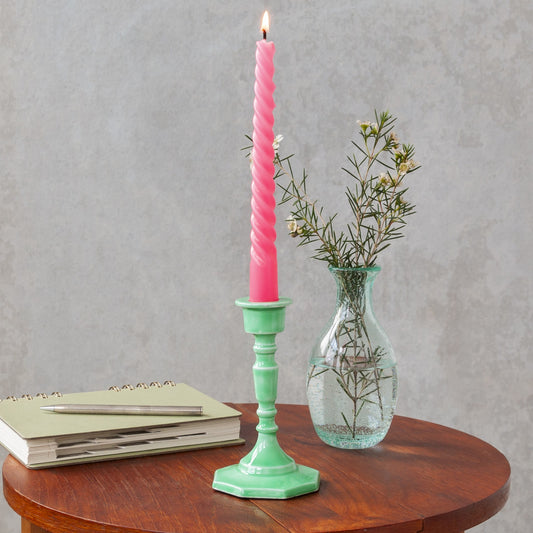 green enamel candlestick with a pink candle on a table next to a vase of flowers and a book