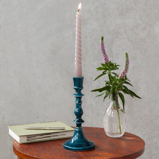 Tall blue enamel candlestick with a pink candle on a table next to a vase of flowers