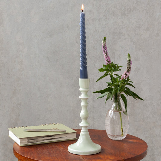 light grey enamel candlestick with a blue candle on a table next to a vase of flowers and a book