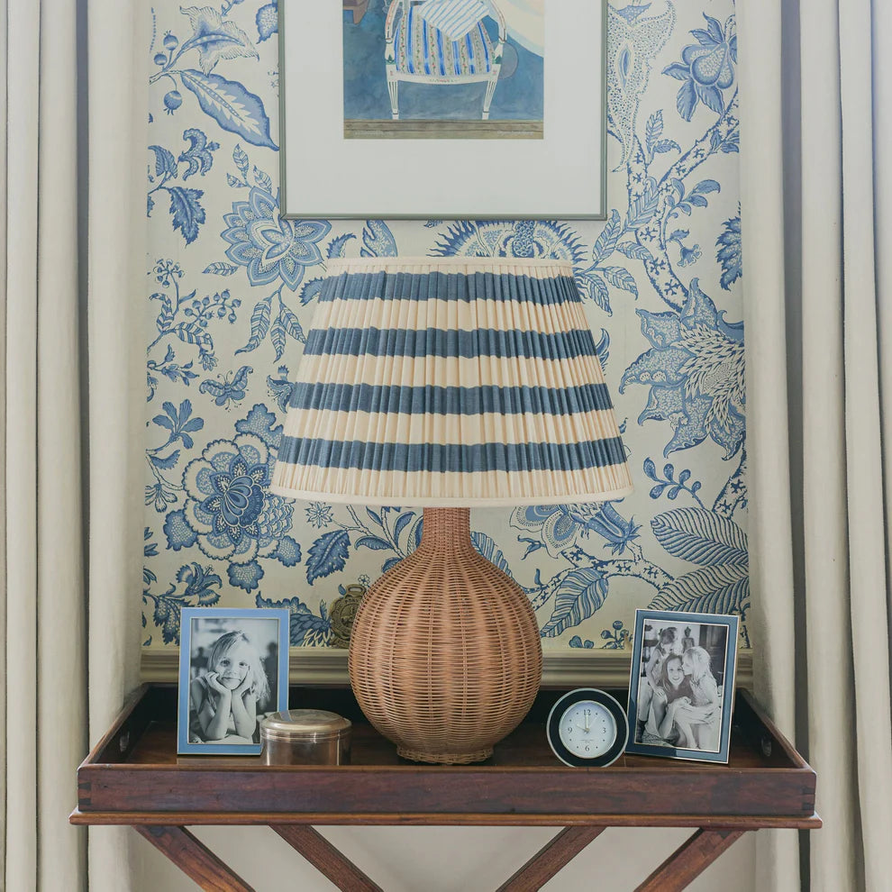 Decorative lamp with striped shade on a wooden tray against floral wallpaper