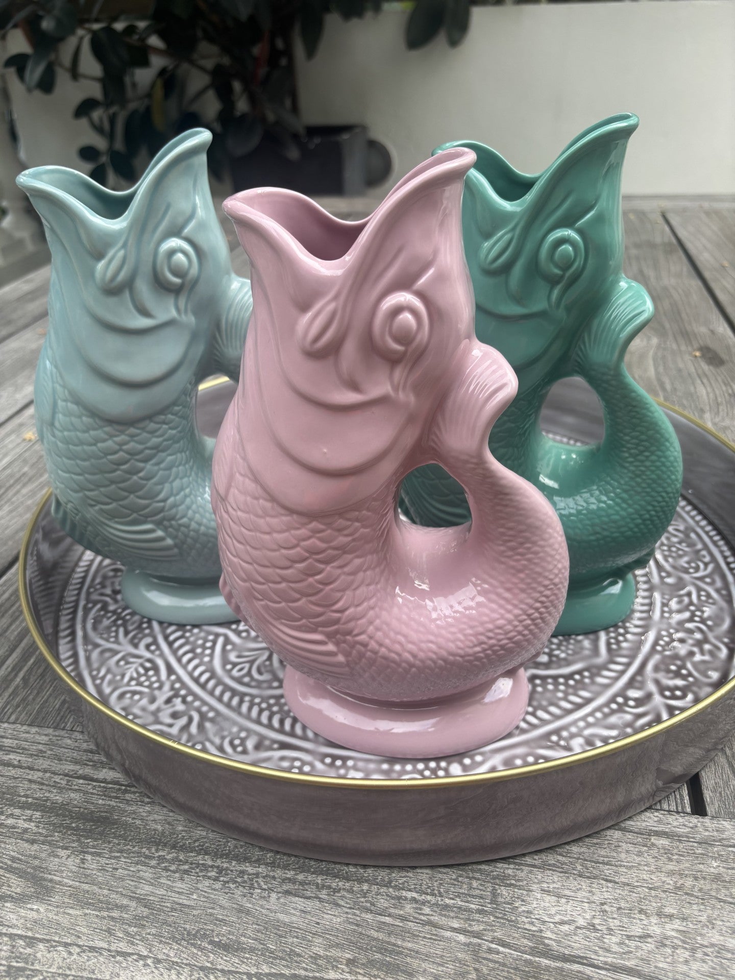 3 ceramic gluggle jugs on a grey tray outside on a table.