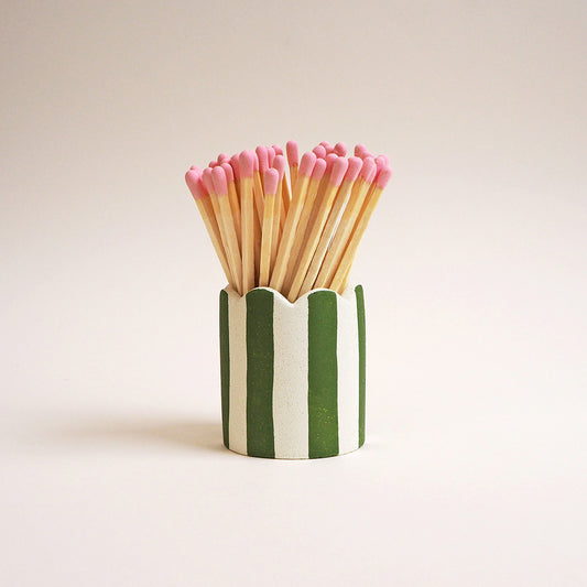 An olive green striped matchstick pot with scalloped edges and pink matches