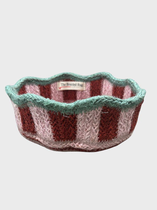 A pink and red striped basket with blue scalloped edging