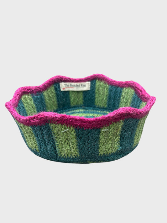 A green and blue striped jute basket with pink scalloped edging
