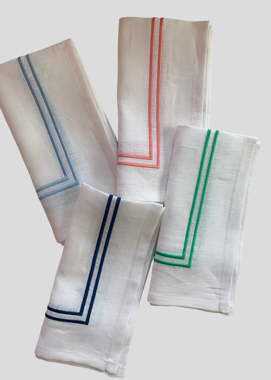 4 white linen napkins with colourful piping around the border