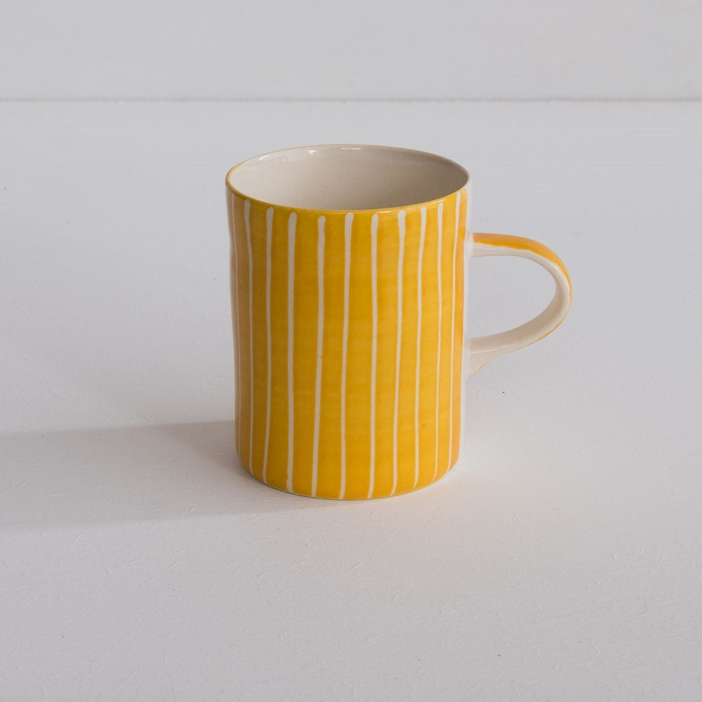 A hand-painted yellow and white mug with sgraffito stripes.