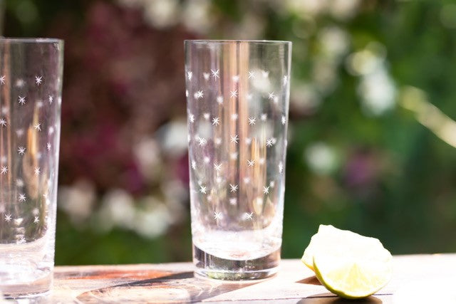 Two crystal highball glasses set on a table outside next to some lemon wedges. The highball glasses have been etched with stars.