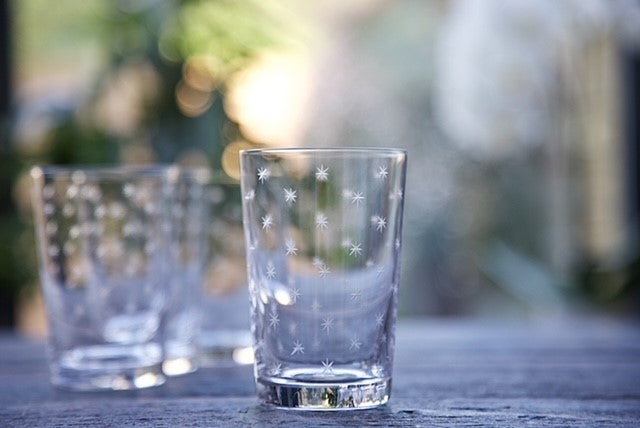 A crystal glass tumbler with a pattern of engraved stars.  There are some other tumblers in the background.