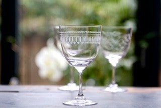 A crystal wine glass with an engraved ovals pattern. There are two other wine glasses in the background.