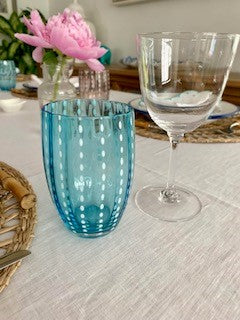 A crystal wine glass with etched stars next to a blue glass tumbler with perlee design.