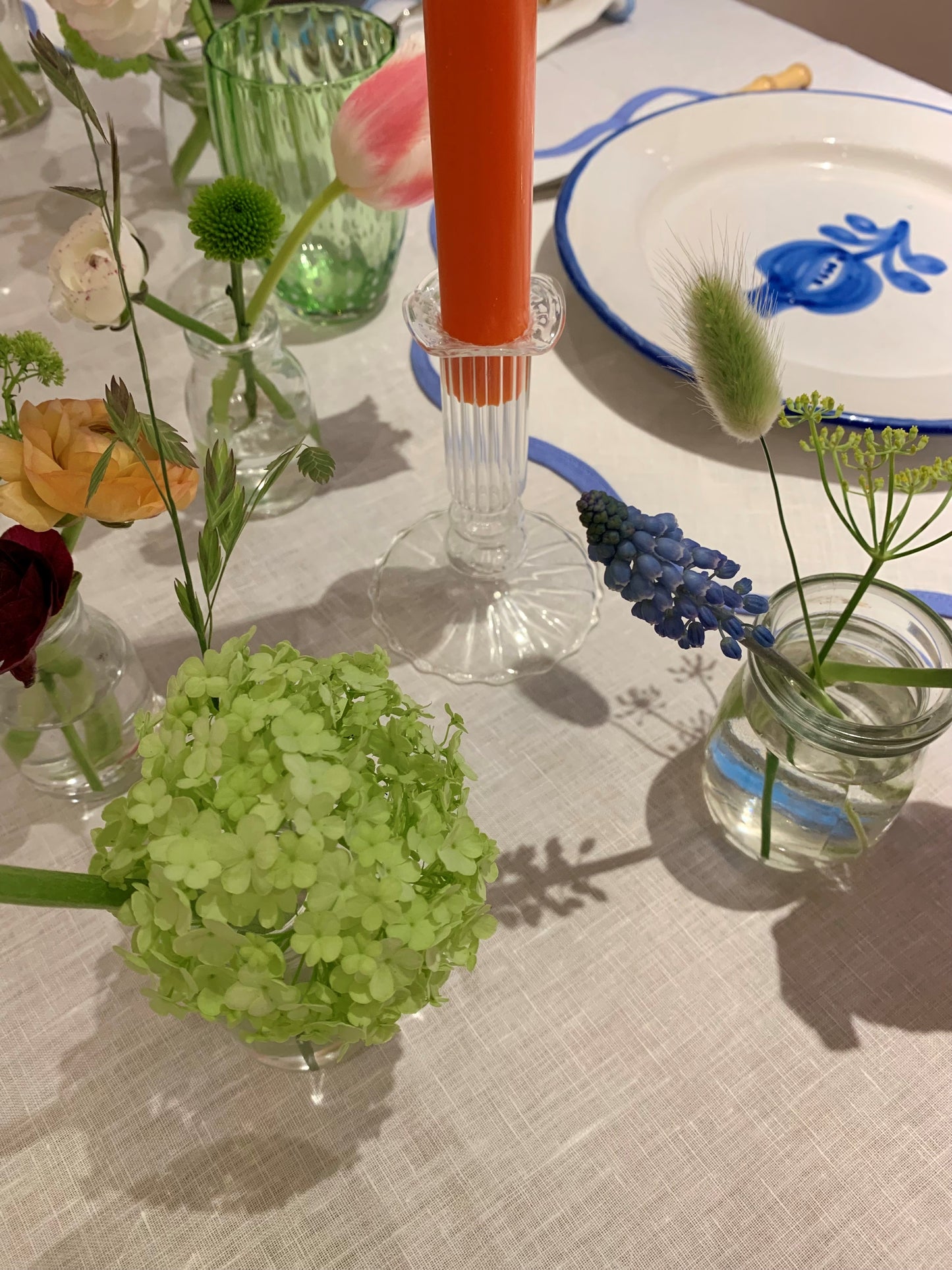 A picture of a laid table with flowers and an orange candle in a short glass candel holder.