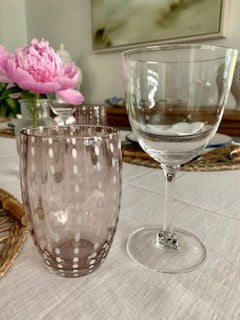 pink glass tumbler with perle design on a table next to a wine glass.