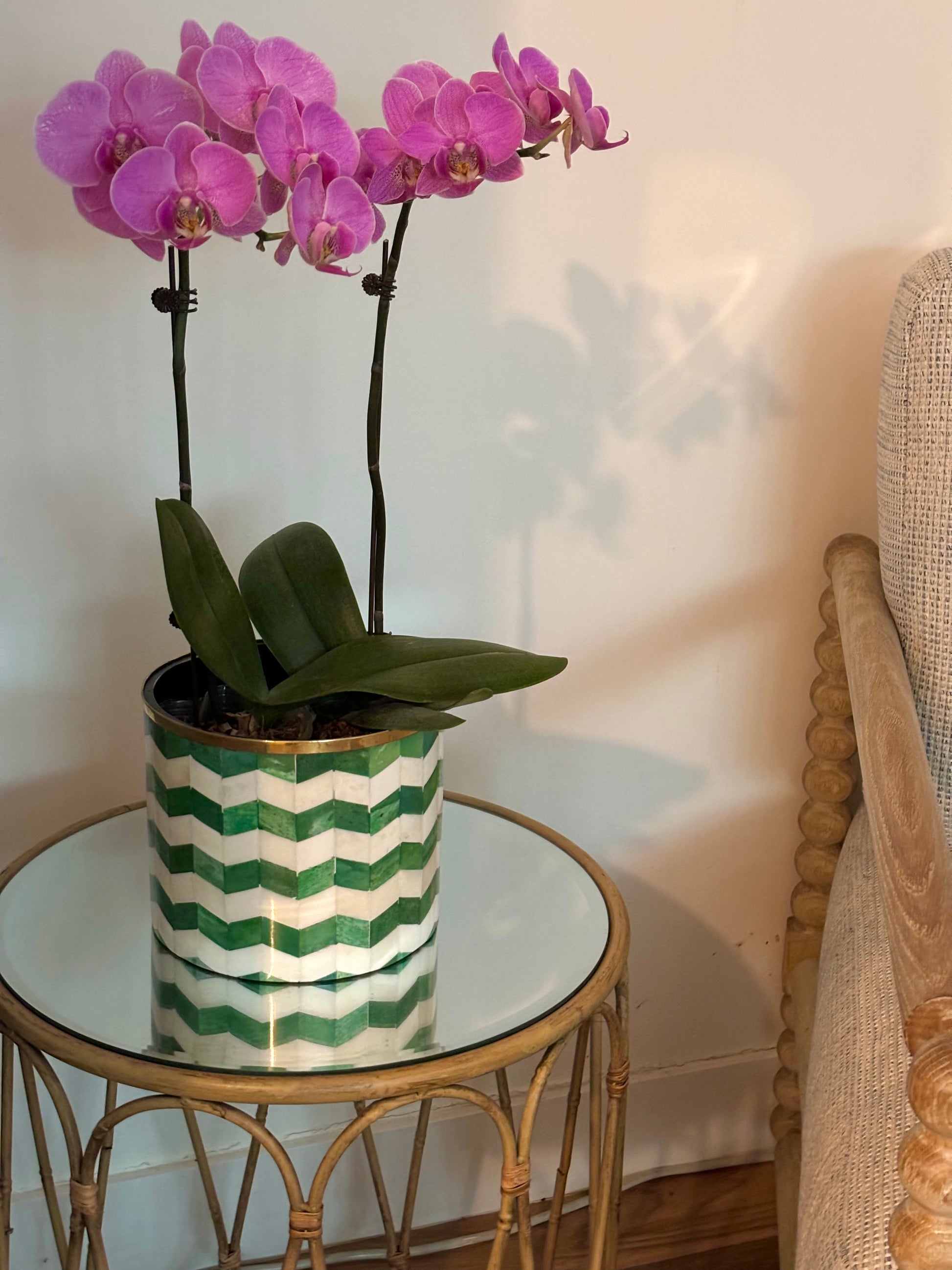 A green and white bone inlay planter with a purple orchid on a bamboo side table.