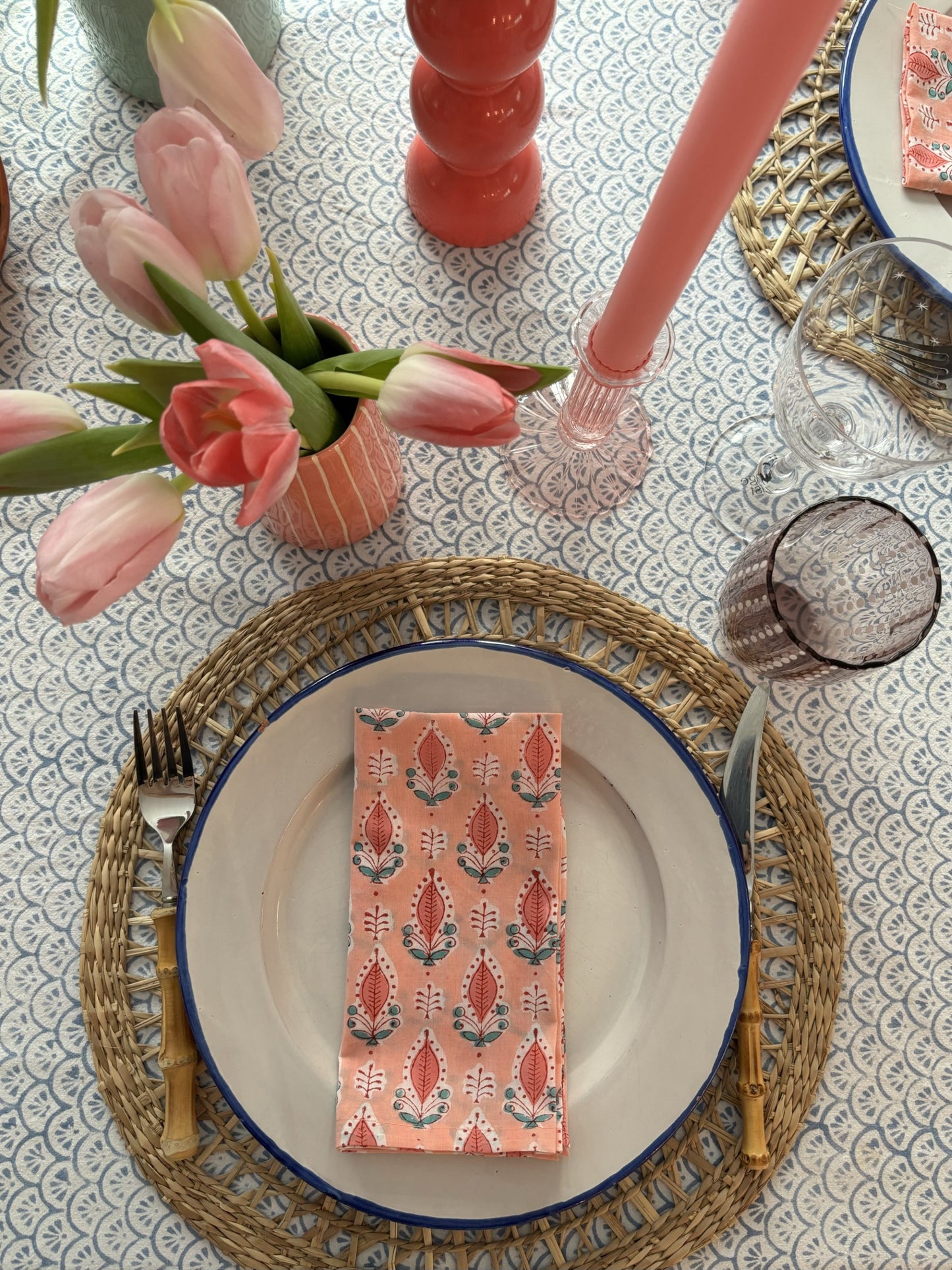 A pink and blue table setting with blockprinted napkins  and a pink vase of tulips.
