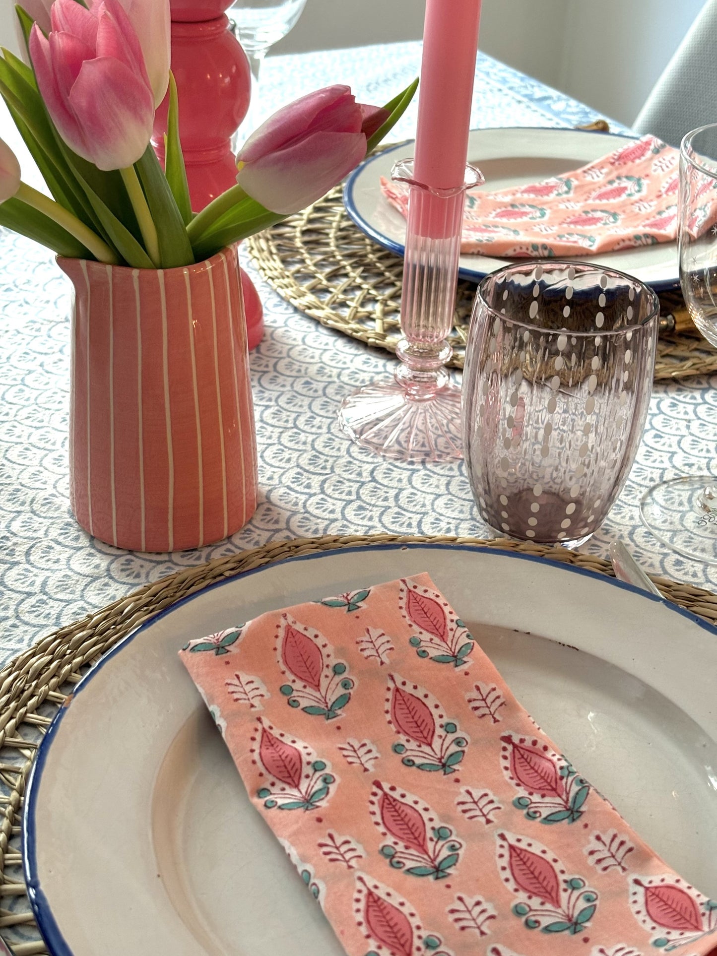A close up of a pink and blue table setting with a pink jug of tulips, pink candles and block printed napkins.