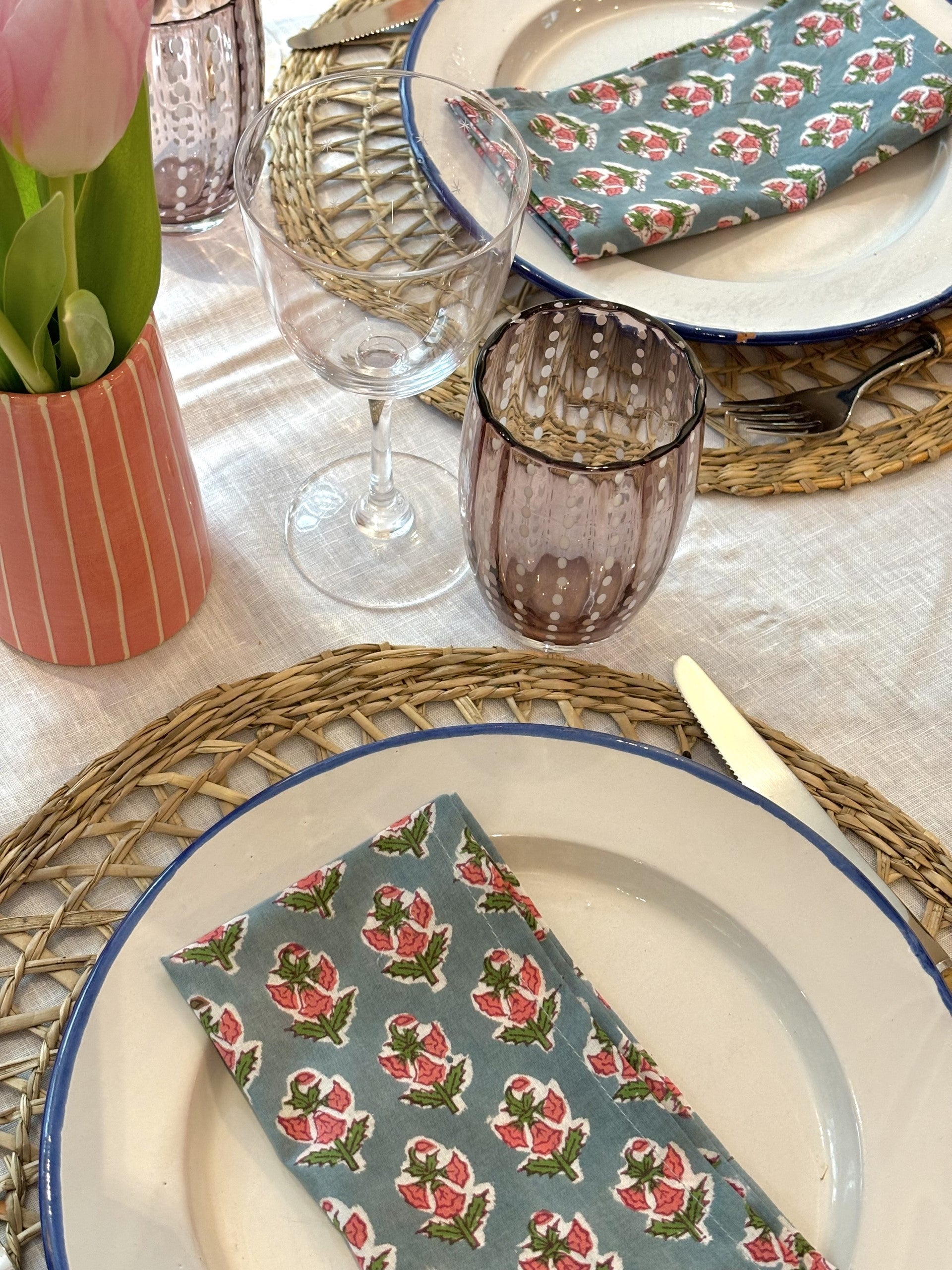 A place setting using wicker placemats and blue and pink floral block printed napkins.