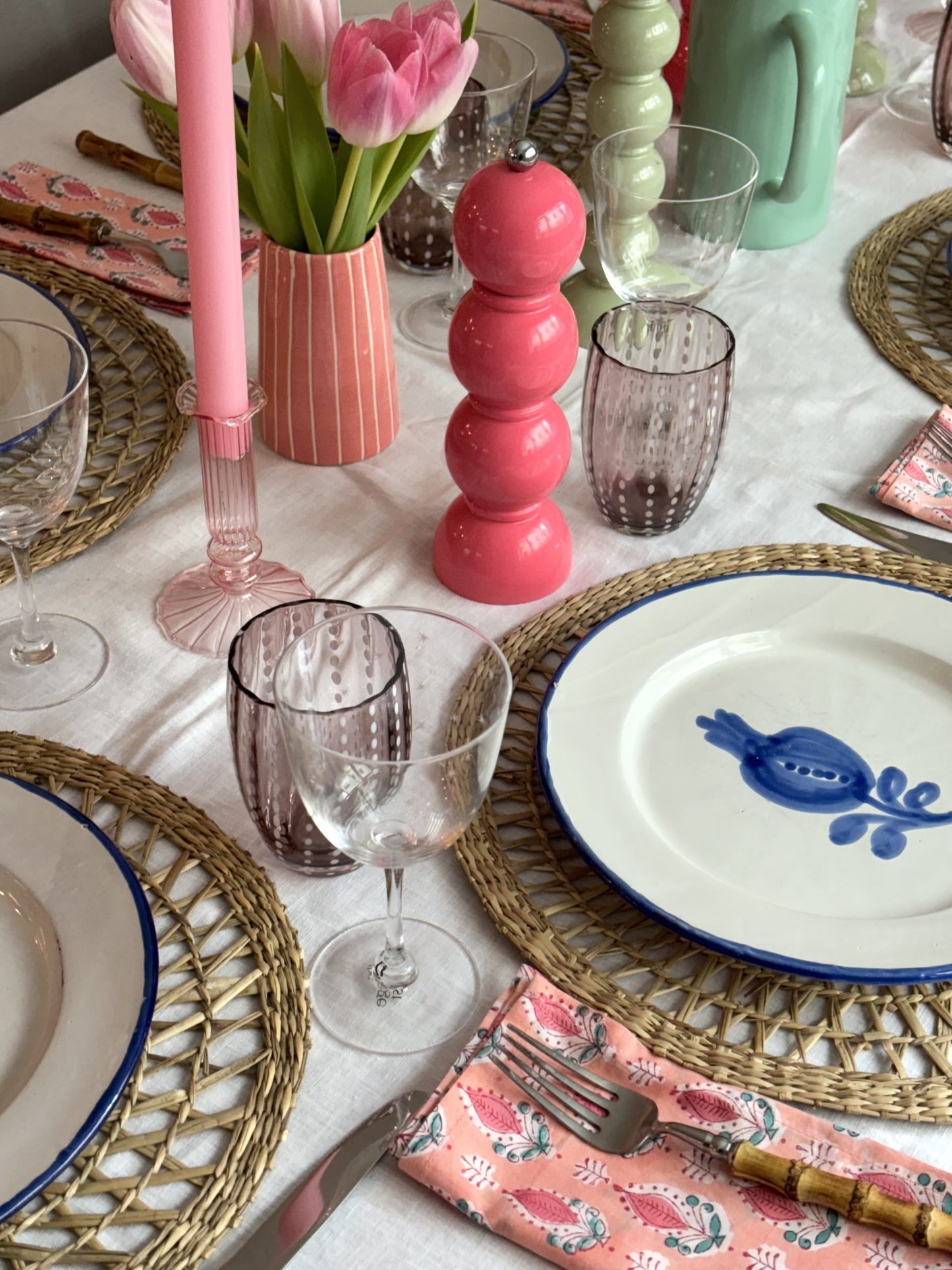 A table setting featuring tulips, pink candles and a watermelon bobbin pepper grinder.