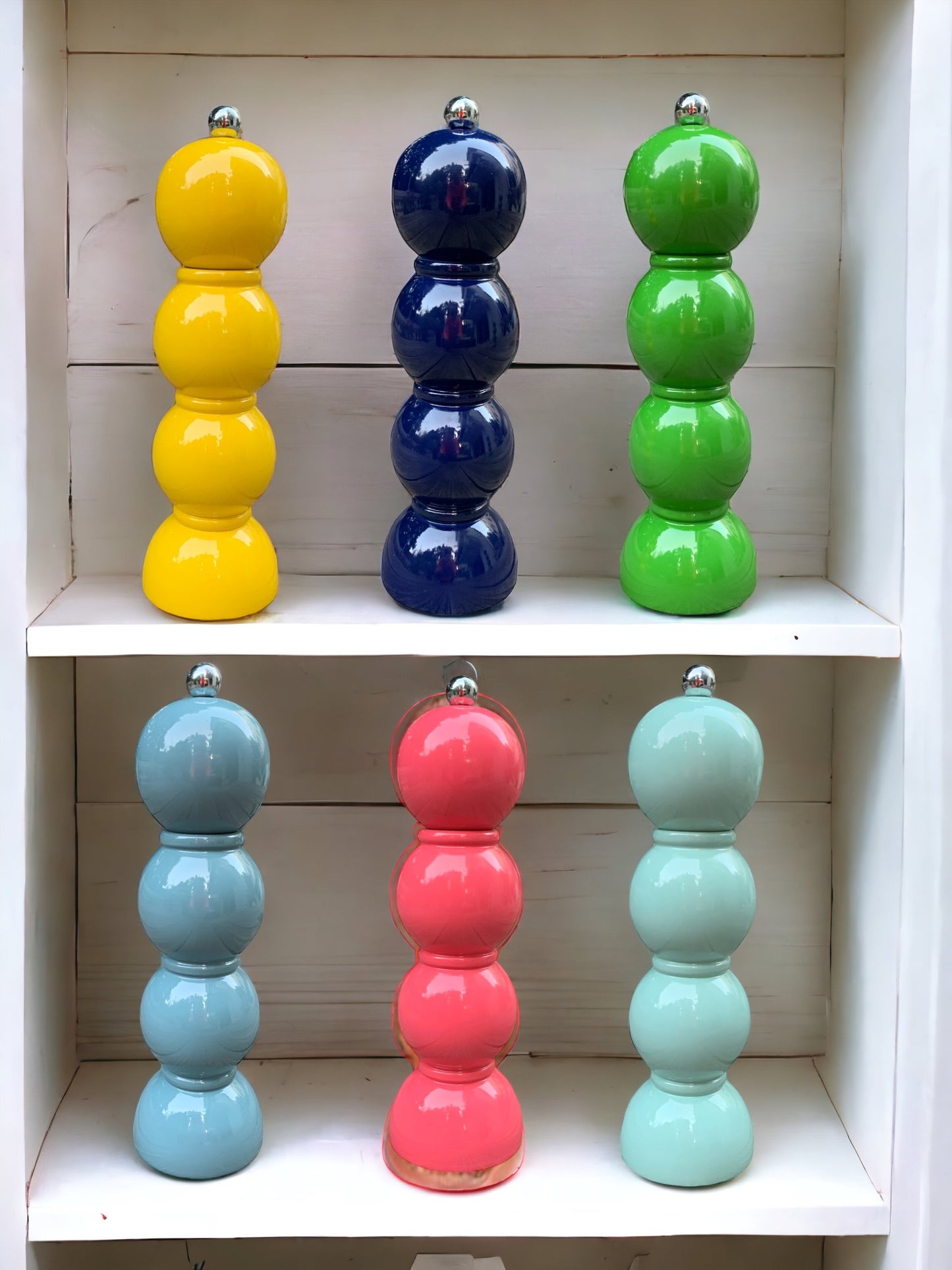 A collection of 6 brightly coloured bobbin pepper grinders on a shelf.
