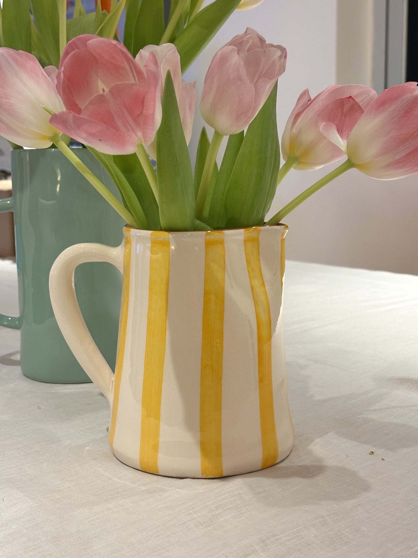 A handpainted yellow and white striped jug with tulips in.