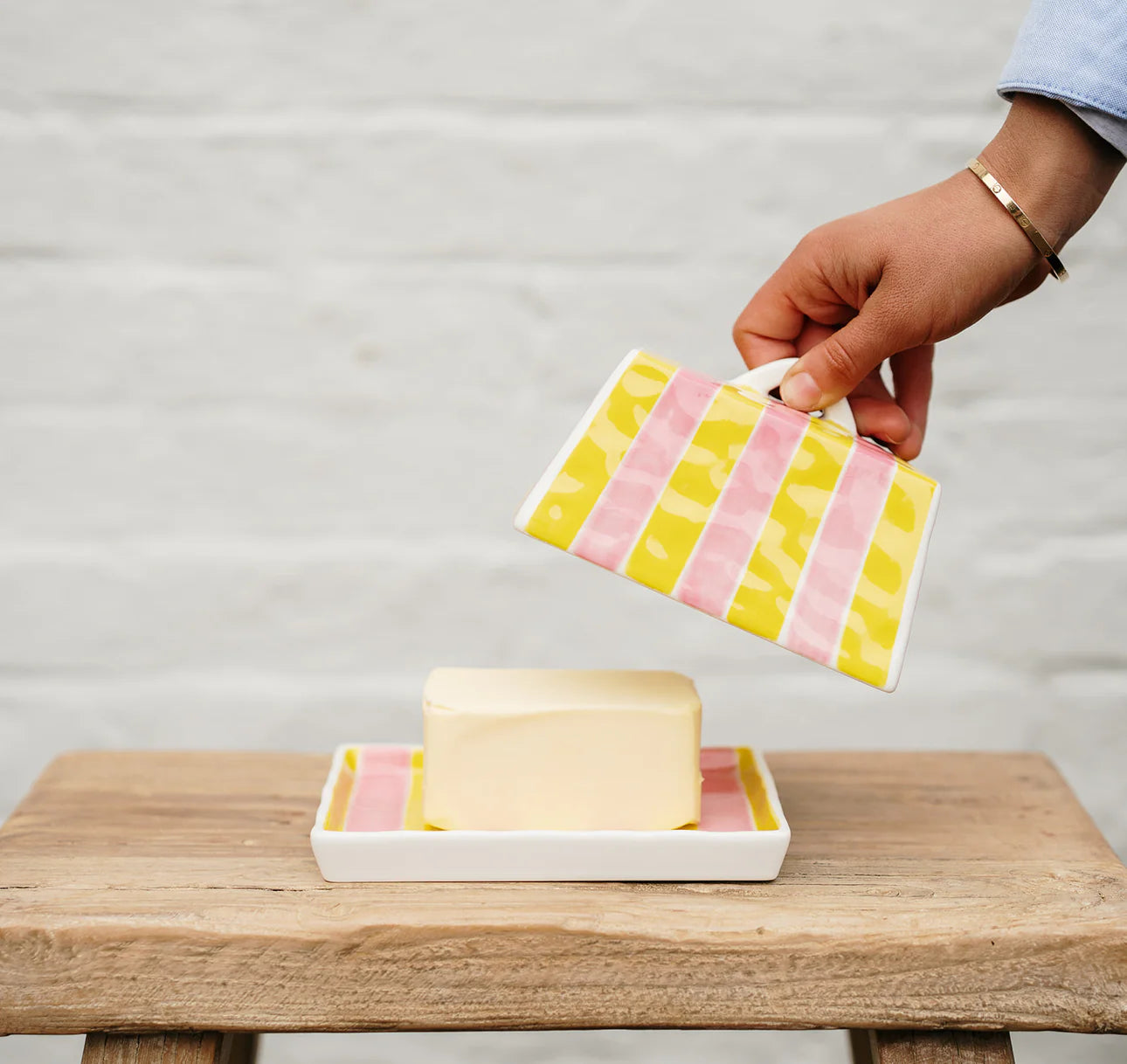 Person holding a colorful striped butter dish over a wooden surface with a white background