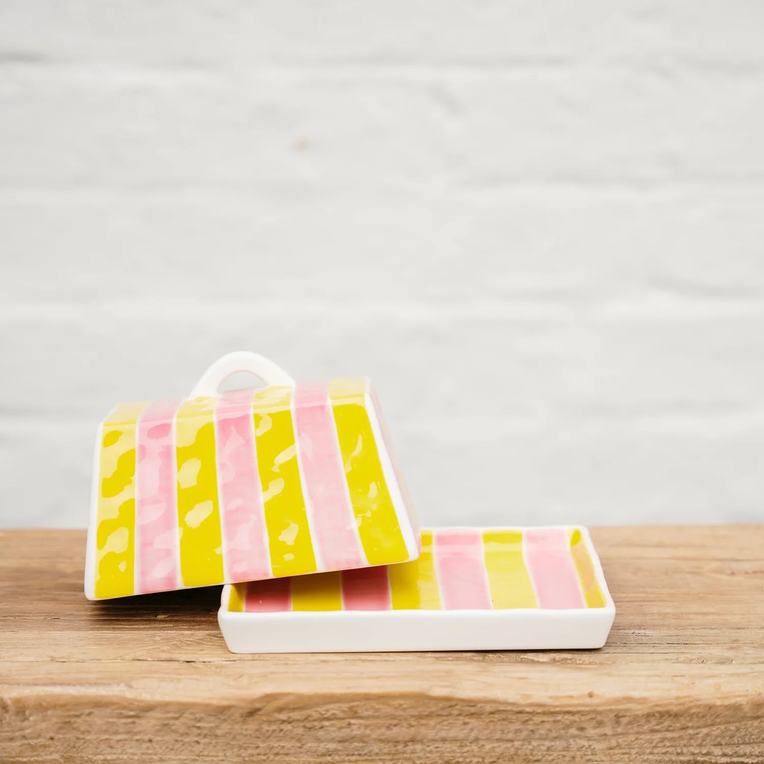 Butter dish with pink and yellow striped patterns on a wooden surface.