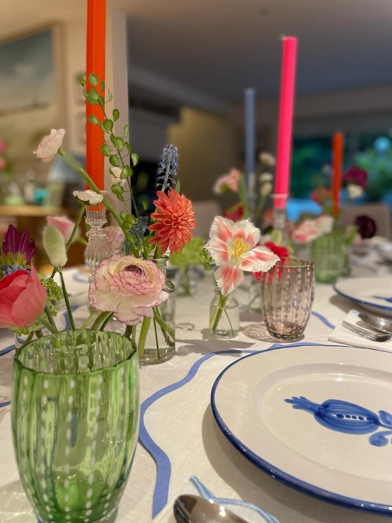 A table setting with lots of little bud vases and pink, blue and orange dinner candles.