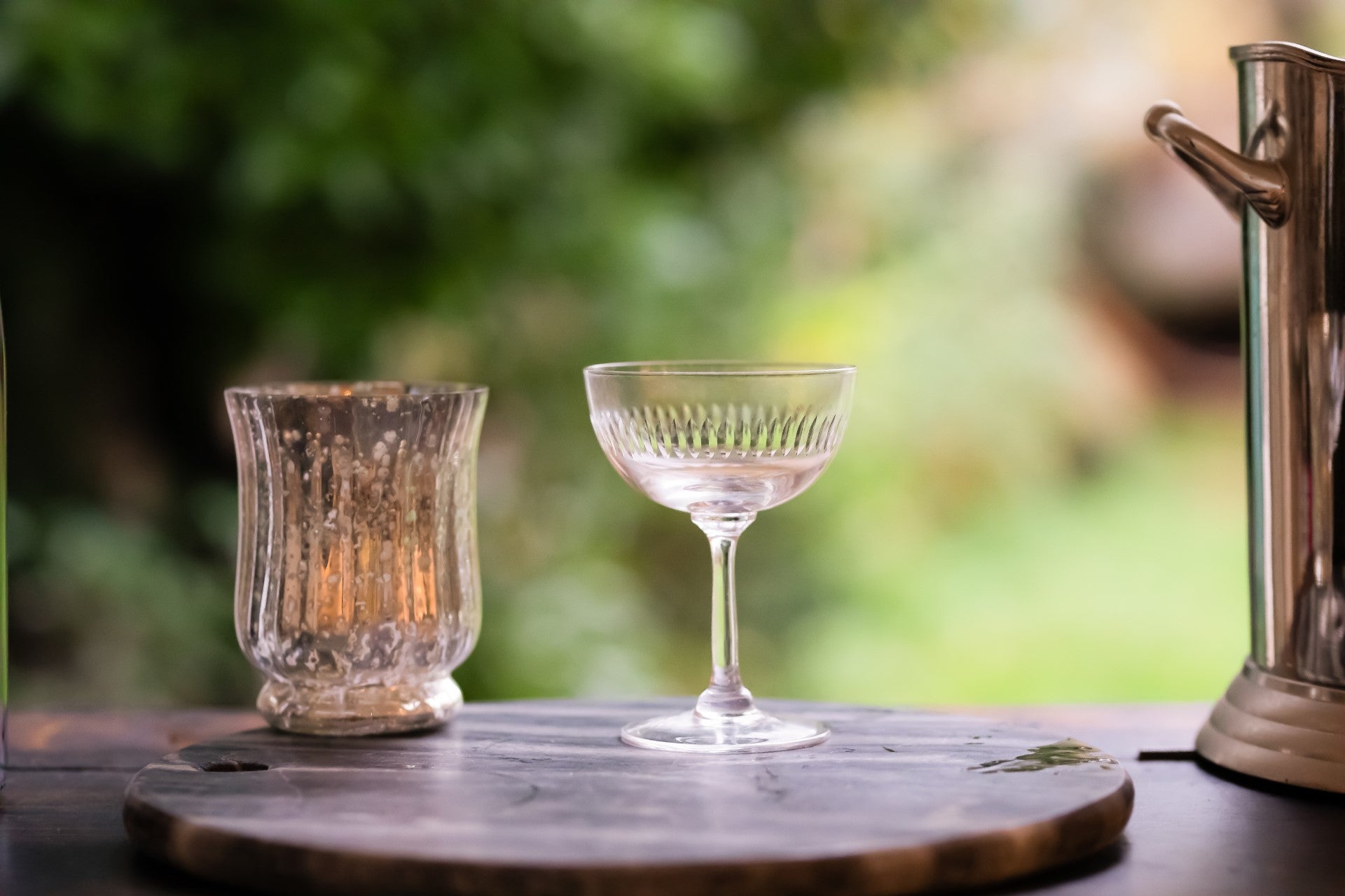 A crystal champagne coupe with a hand-cut spears design on a table next to a candle and a champagne bucket.