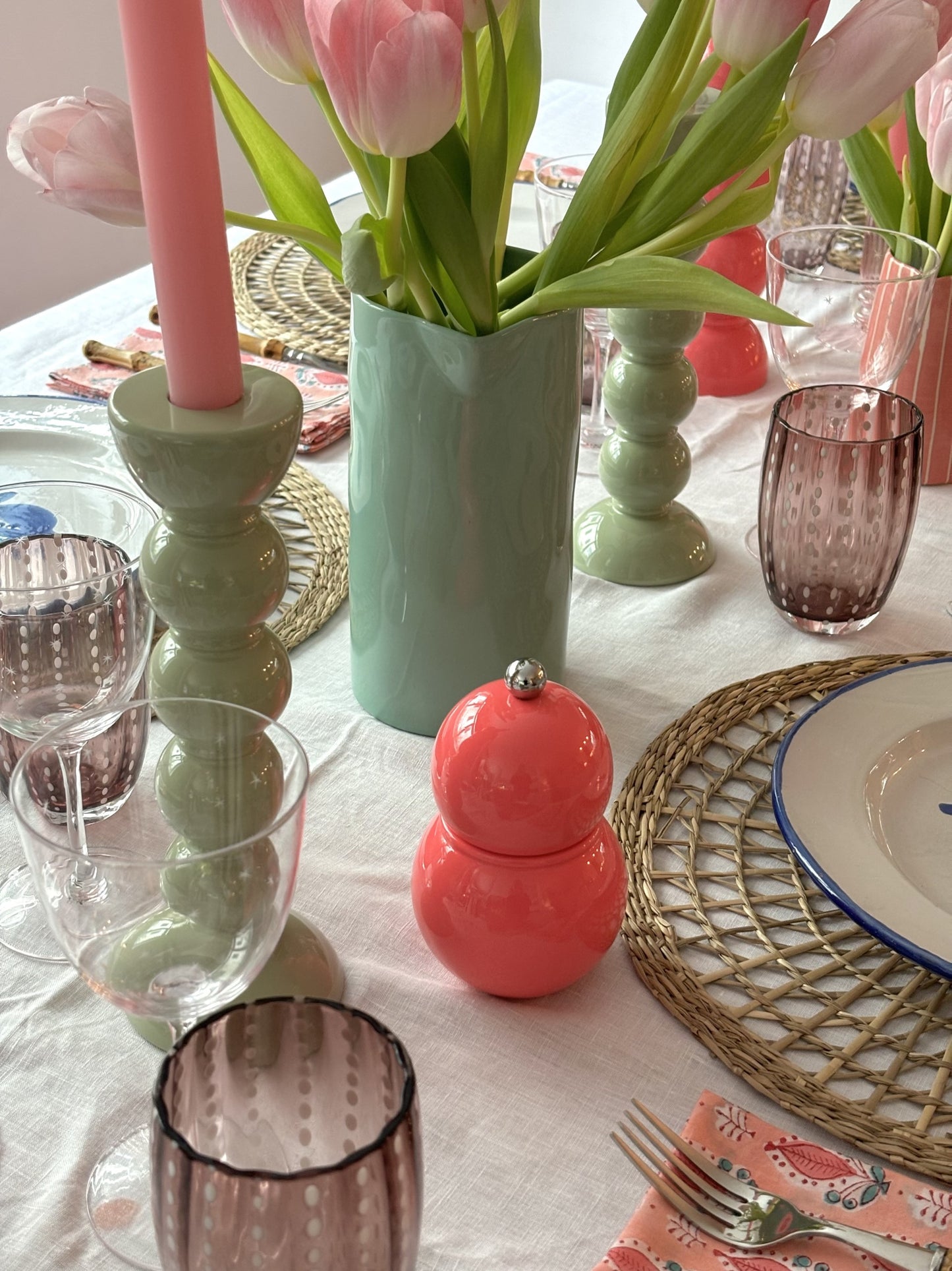 A tablescape with sage bobbin candlesticks and a pink coloured Chubbie salt and pepper grinder.  There is also a green jug with tulips in the middle of the table.