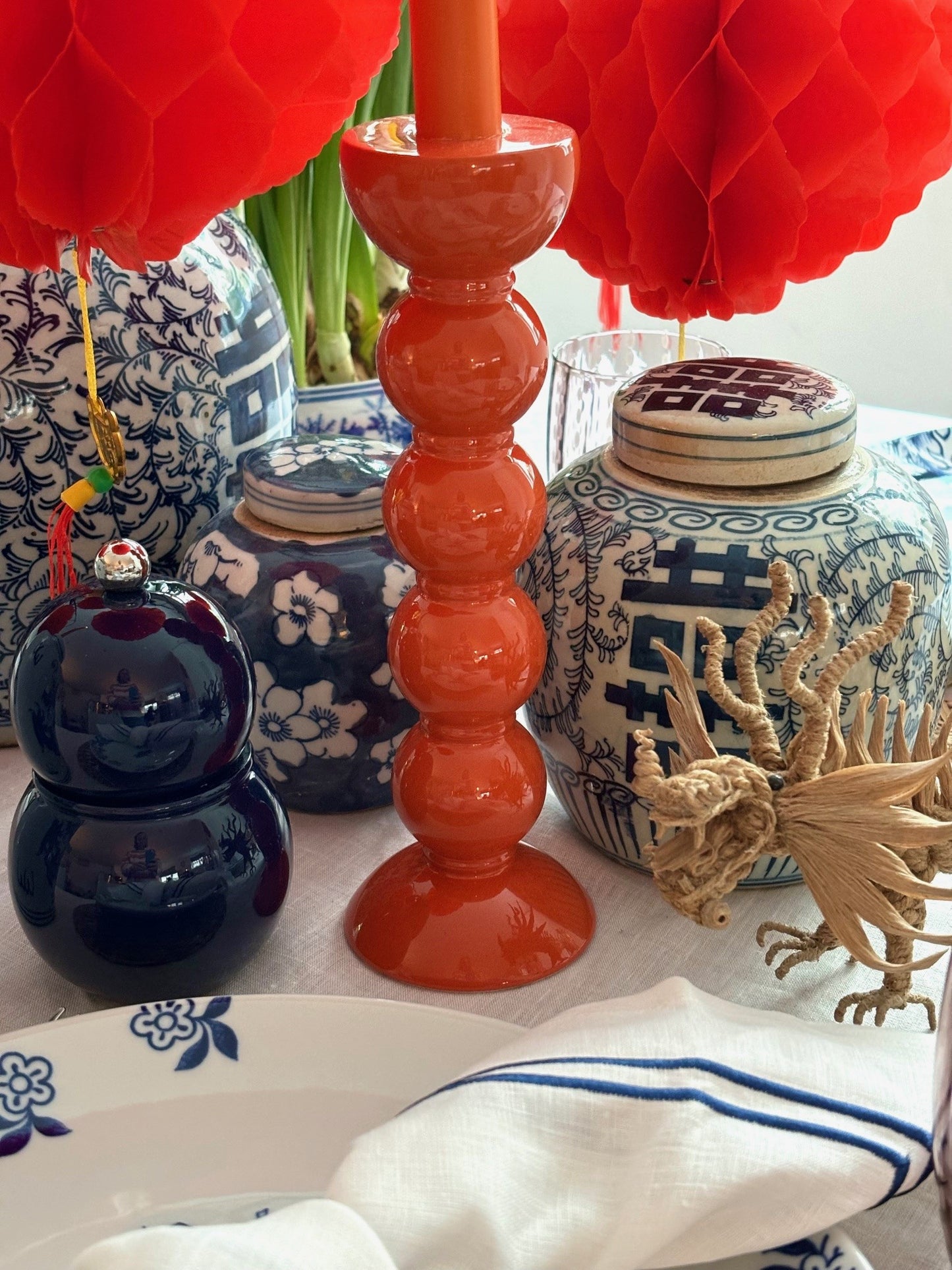 A Chinese New Year table setting featuring blue and white ginger jars, an orange candlestick and a navy blue chubbie pepper grinder.