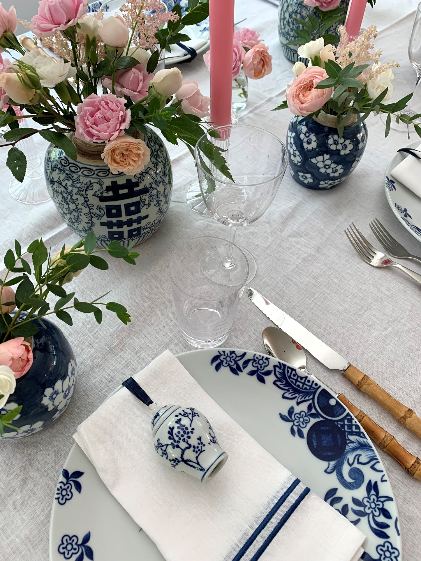 A blue and white tablescape featuring small blue and white ginger jars filled with pink flowers.