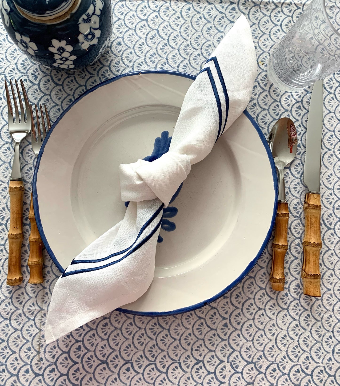 A blue and white place setting with a knotted linen napkin with dark blue piping.
