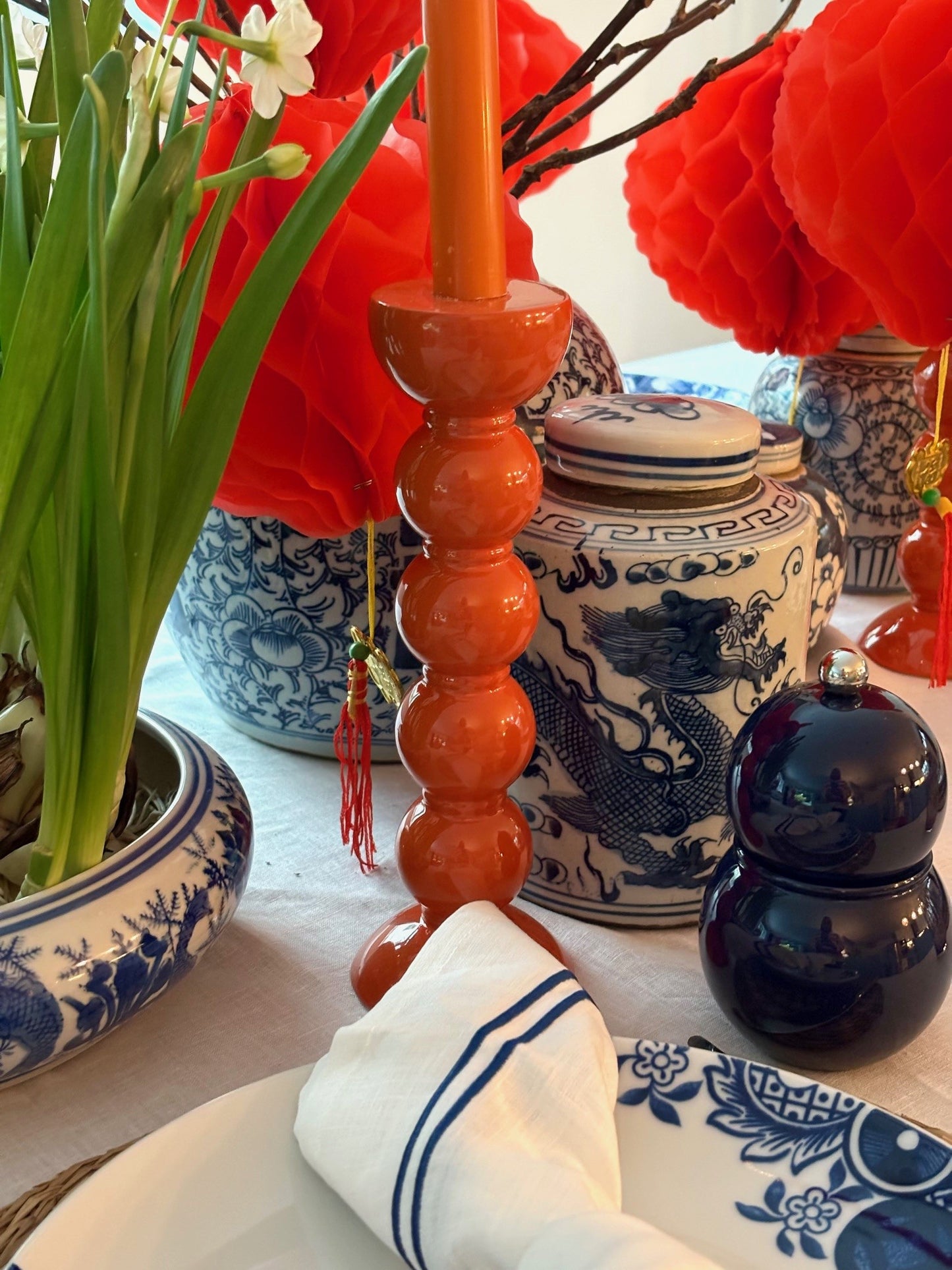 A Chinese New Year table setting featuring a blue and white dragon ginger jar and an orange candlestick and narcissus flowers.