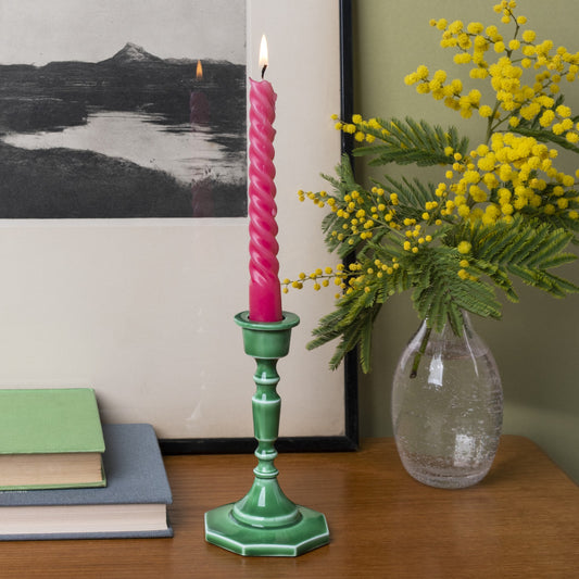 dark green enamel candlestick with a pin candle on a shelf next to a vase of flowers
