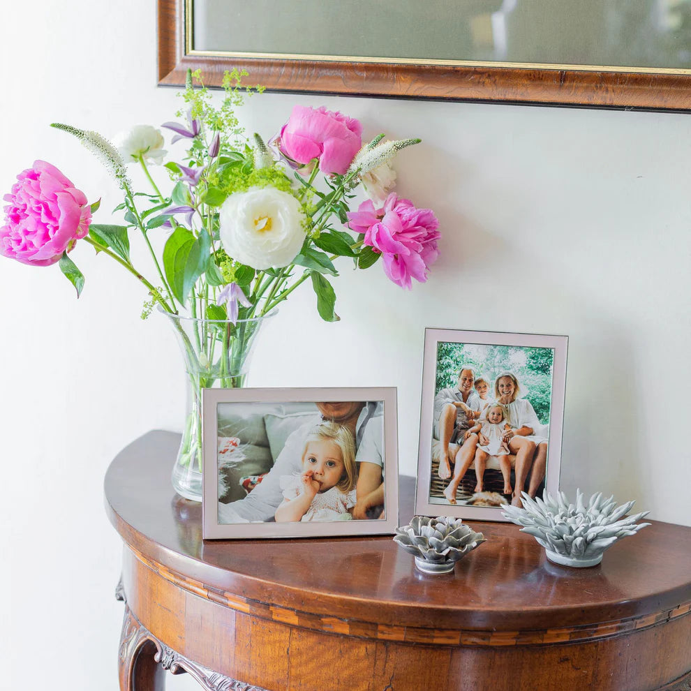 Decorative table with flowers, family photos, and small plants against a white wall.