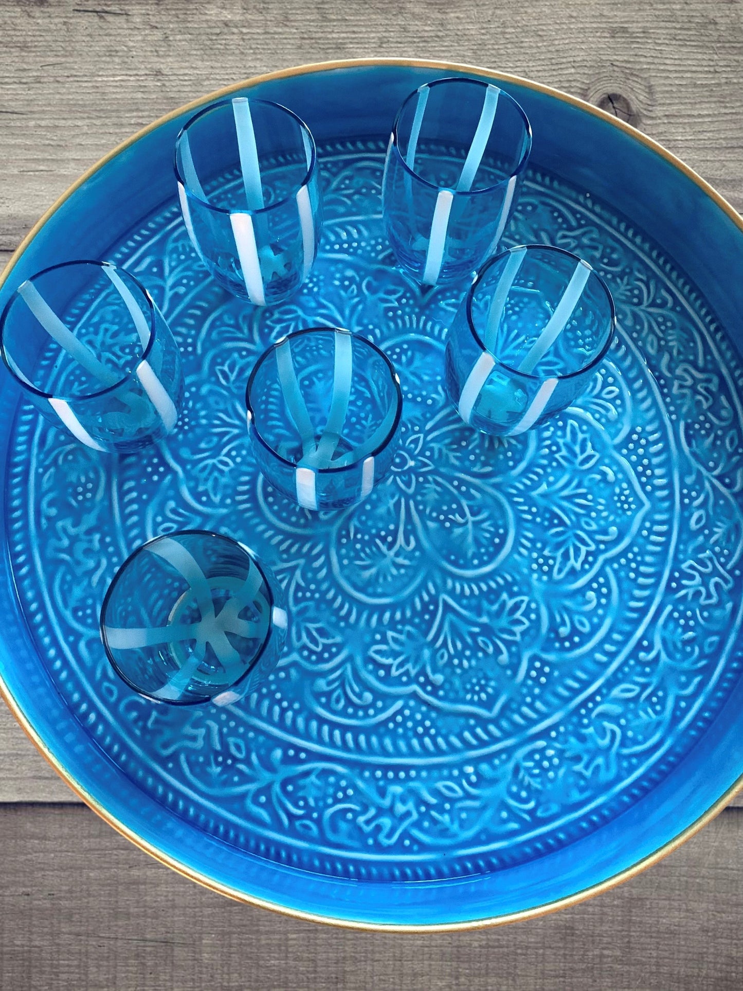 A blue enamel tray on a table with 6 blue and white striped glass tumblers.