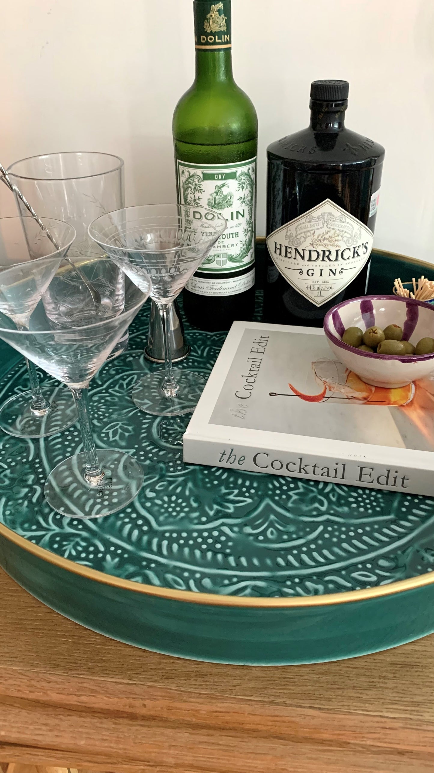 A teal coloured enamel drinks tray with a cocktail book, martini glasses and some spirits.