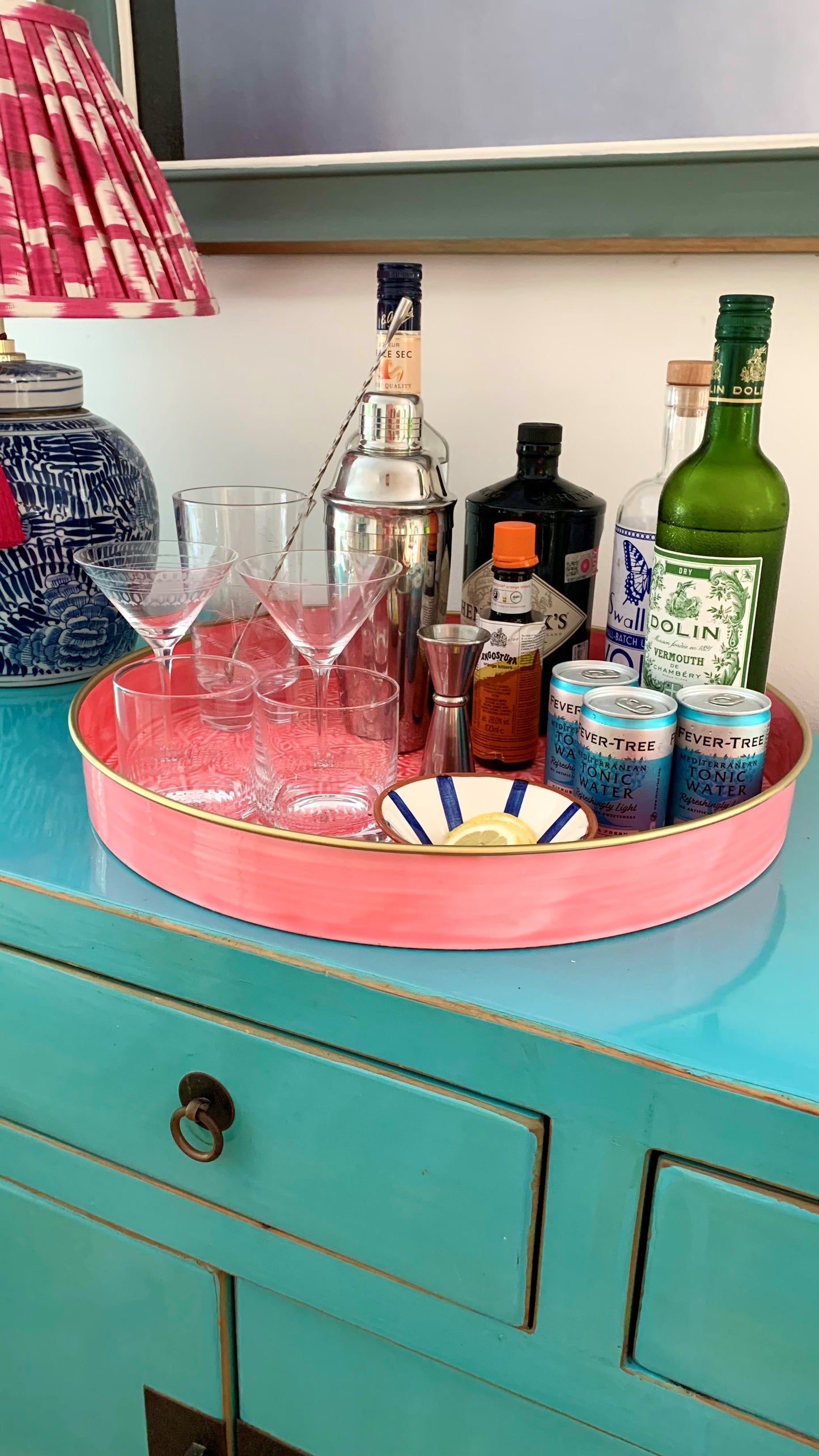 A bright pink tray being used as a drinks tray on a turquoise sideboard.