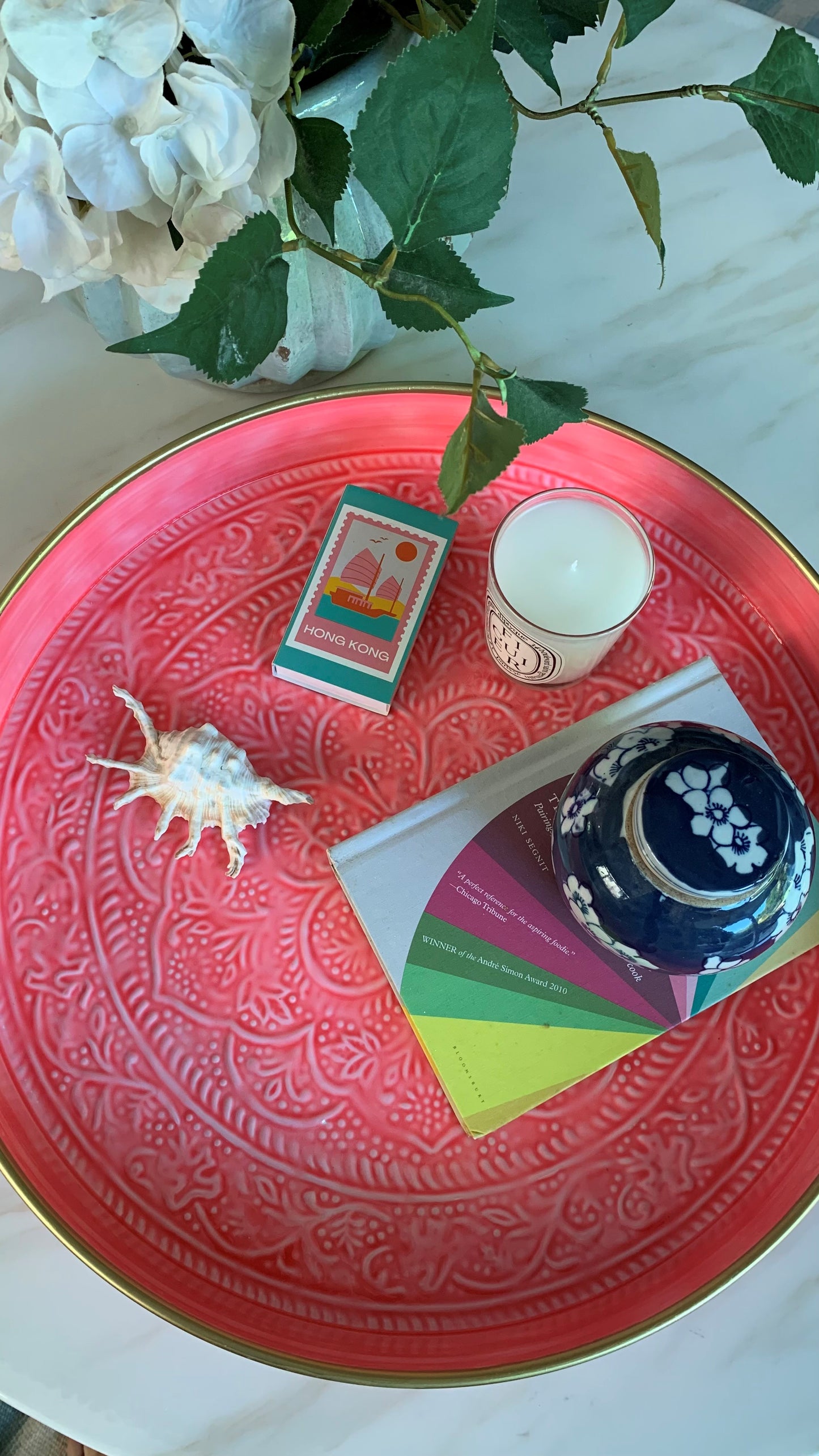 A large pink tray displayed on a coffee table with a candle, book, ginger jar and shell