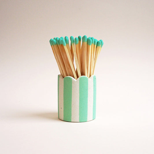 A mint striped matchstick pot with scalloped edges filled with long matches
