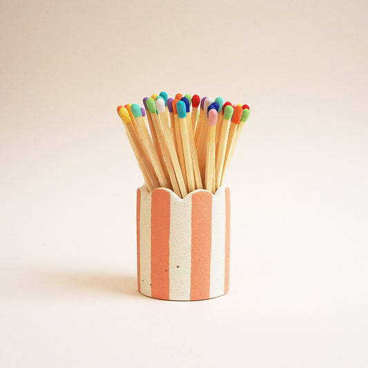 A peach striped matchstick pot with scalloped edges and rainbow colour matches