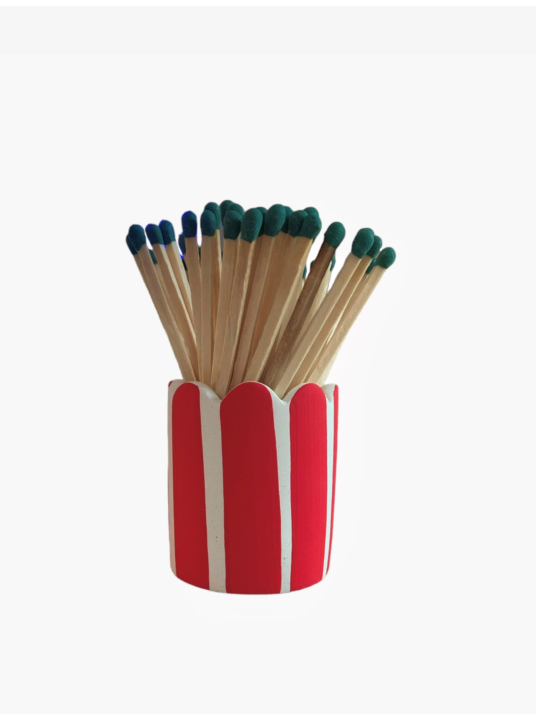 A red and white striped matchstick pot with scalloped edges and green matches.