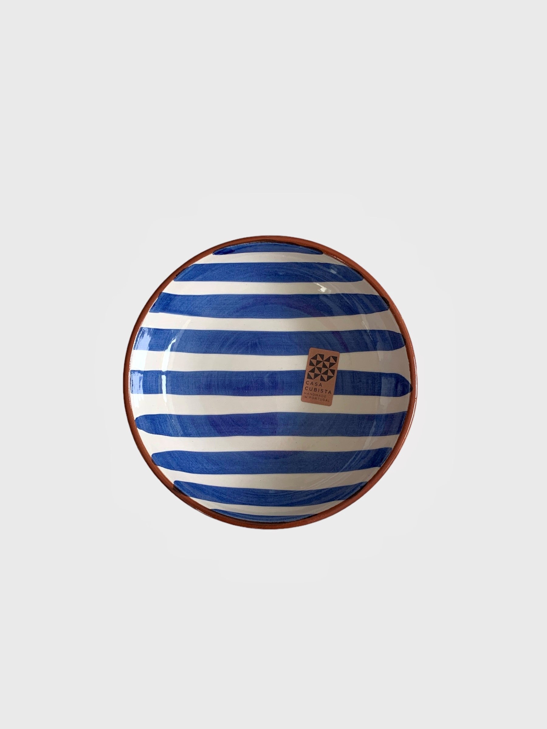 A small ceramic bowl with hand-painted bold blue stripes on it.  Made in Portugal from casa cubista