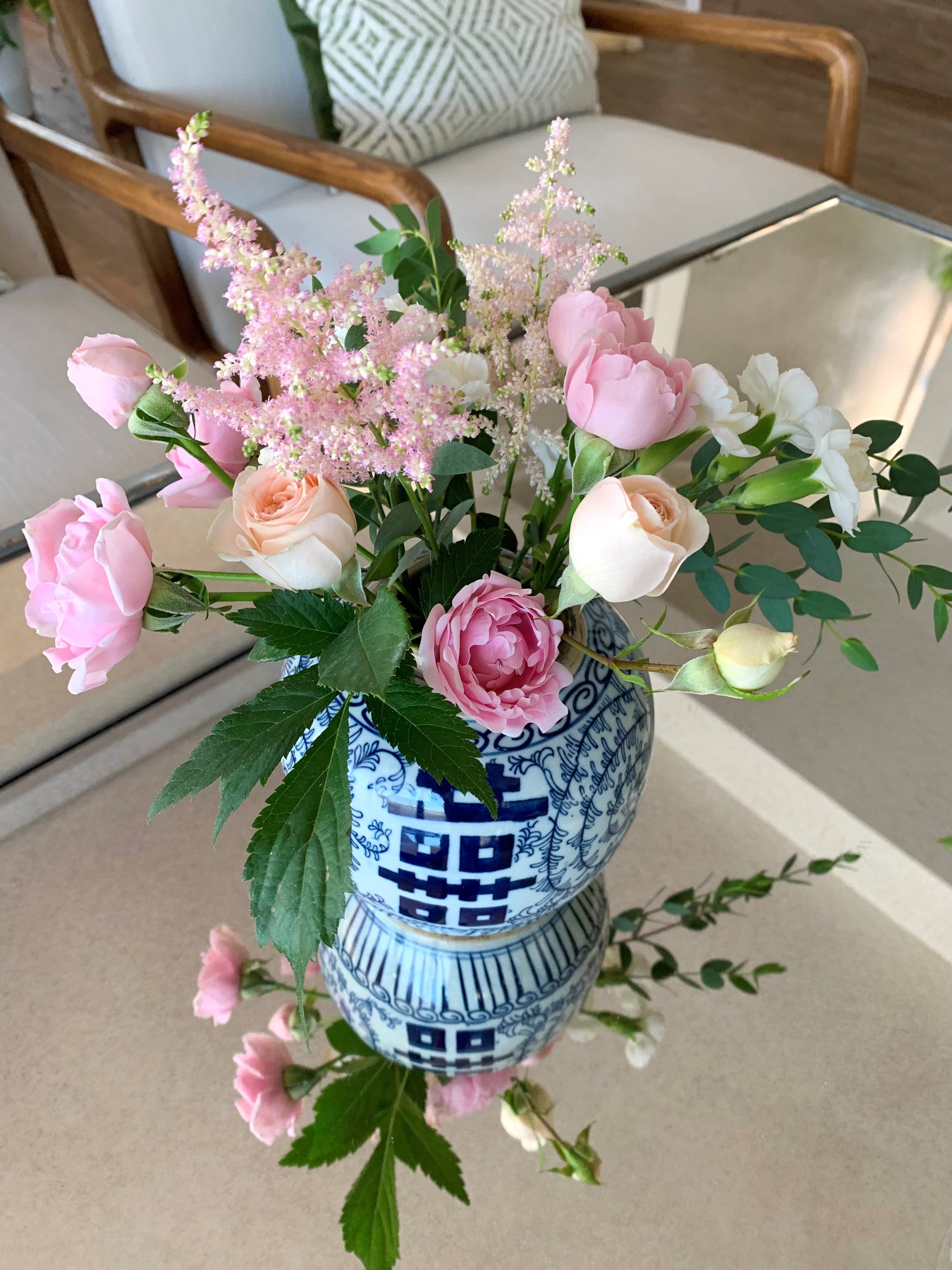 A medium double happiness ginger jar filled with pink flowers on a coffee table.