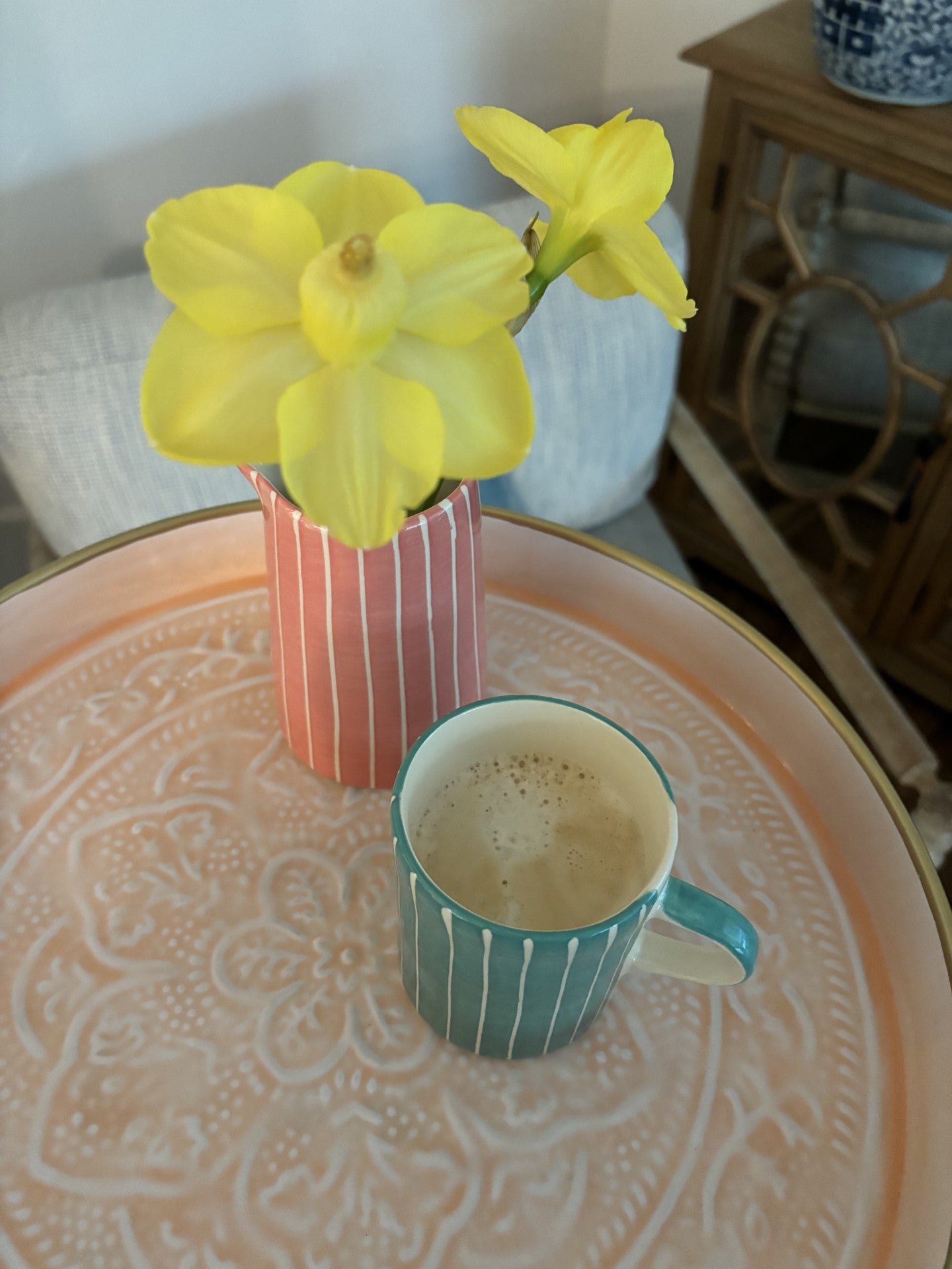 A light pink enamel tray with a pink vase of daffodils and a cup of coffee.