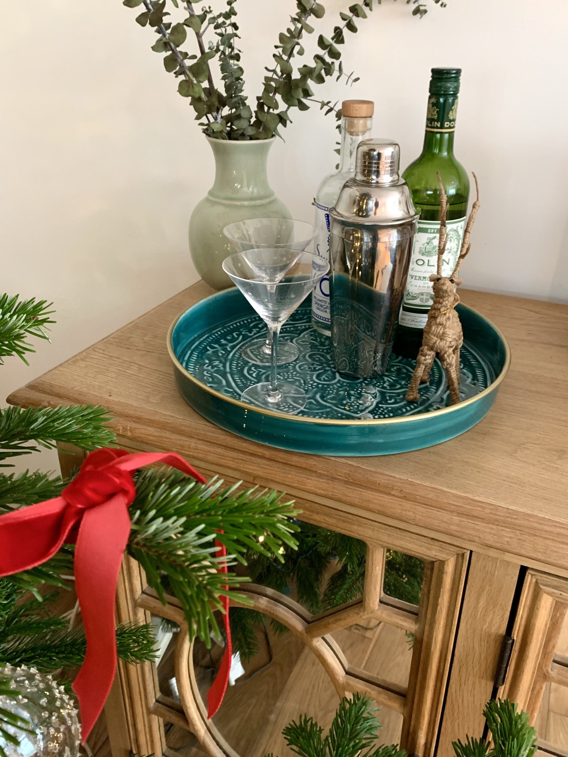 A medium sized teal tray on a sideboard with 2 martini glasses, a cocktail shaker and 2 bottles of spirits.