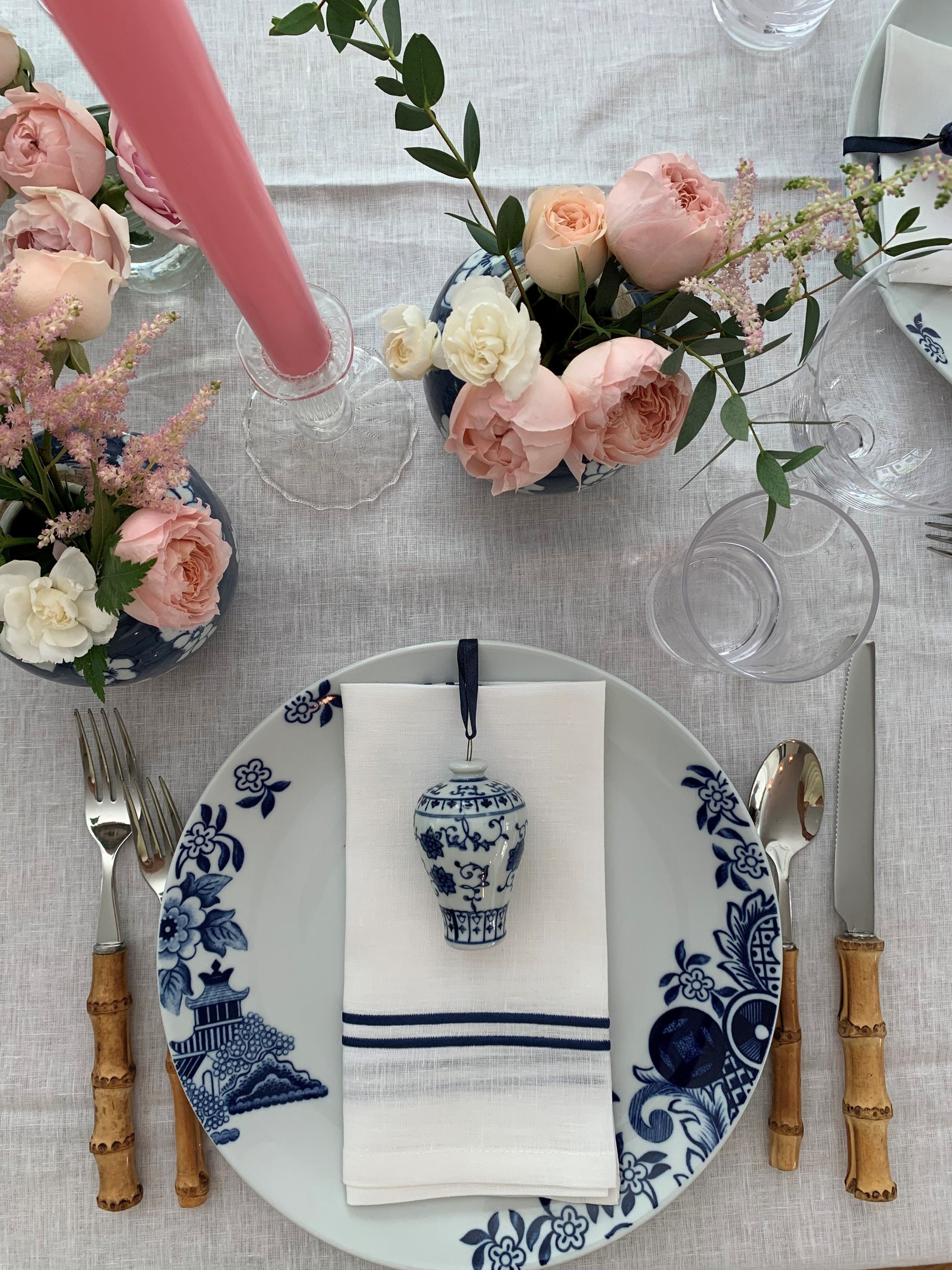 A place setting featuring pink flowers and candles and mini ginger jars